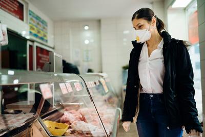 Женщина в медицинской маске перед витриной с продуктами 